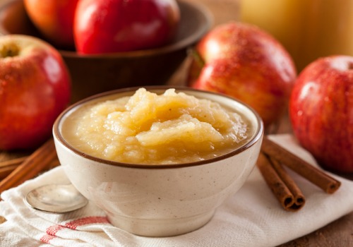 Bowl of apple sauce sitting near some cinnamon sticks.