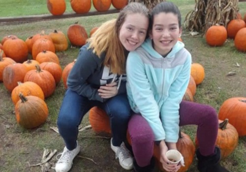 Two girls sit and smile in the Pumpkin patch for Freeport IL residents, which is located at Tanners Orchard