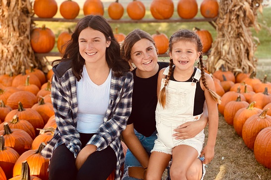 A young family sits and smiles among pumpkins at Tanners Orchard, which offers Family Fun for Joliet IL residents