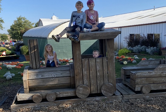 Kids pose on a wooden train at Tanners Orchard, which offers numerous Kids Activities for Aurora IL residents