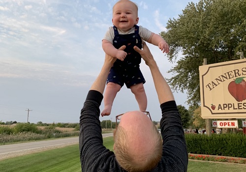 A man holds his baby in the air after enjoying a day at Tanners Orchard, an Apple Picking Farm Dunlap IL residents can enjoy