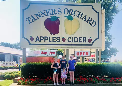 A family poses in front of a Tanners Orchard sign. If you're asking "What Should You Look for When Picking Apples" trust the experts at Tanners Orchard.