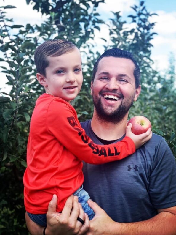 A man and his son smile at the camera with a freshly picked apple from Tanners Orchard, which offers farm attractions & activities in Illinois