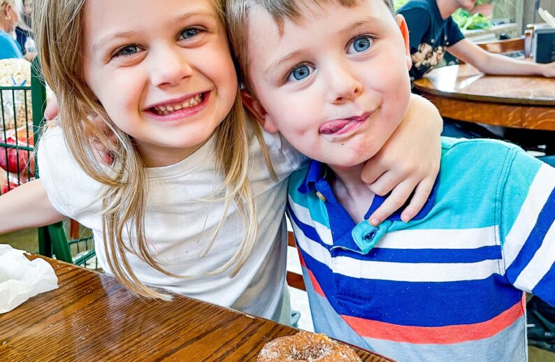 Children smile and pose for the camera with an apple cider donut from Tanners Orchard, which offers farm attractions & activities in Illinois