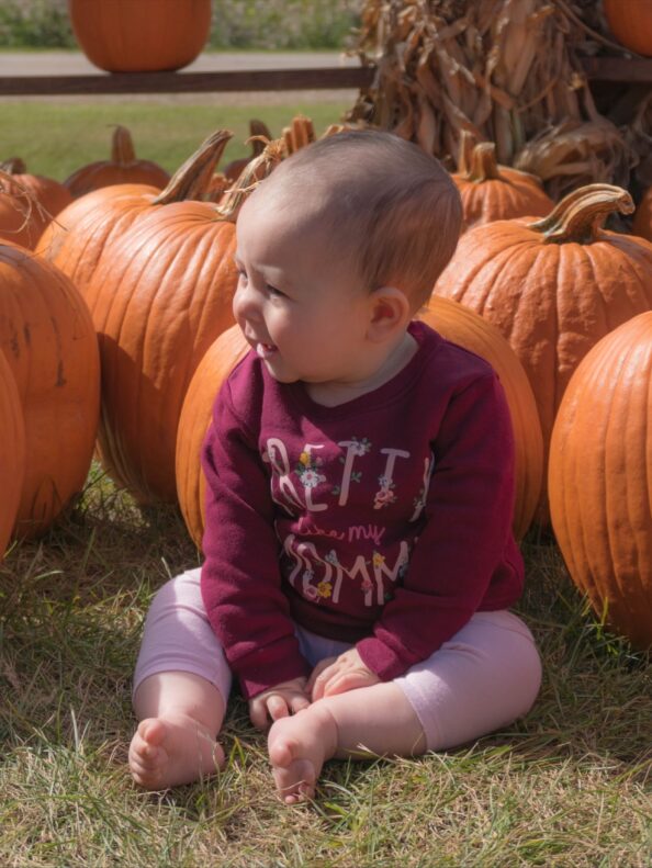 A baby sits among pumpkins at Tanners Orchard, which offers farm attractions & activities in Illinois