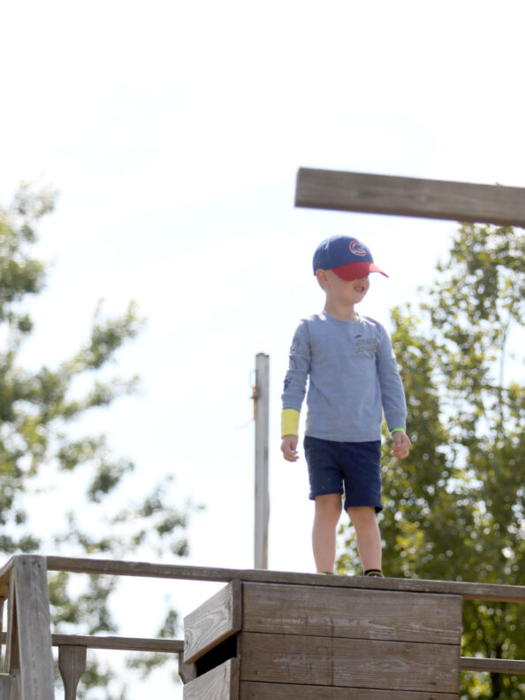 A young boy standing tall on one of the wooden climbable features part of the Back 40 Fun Acres at Tanners Orchard