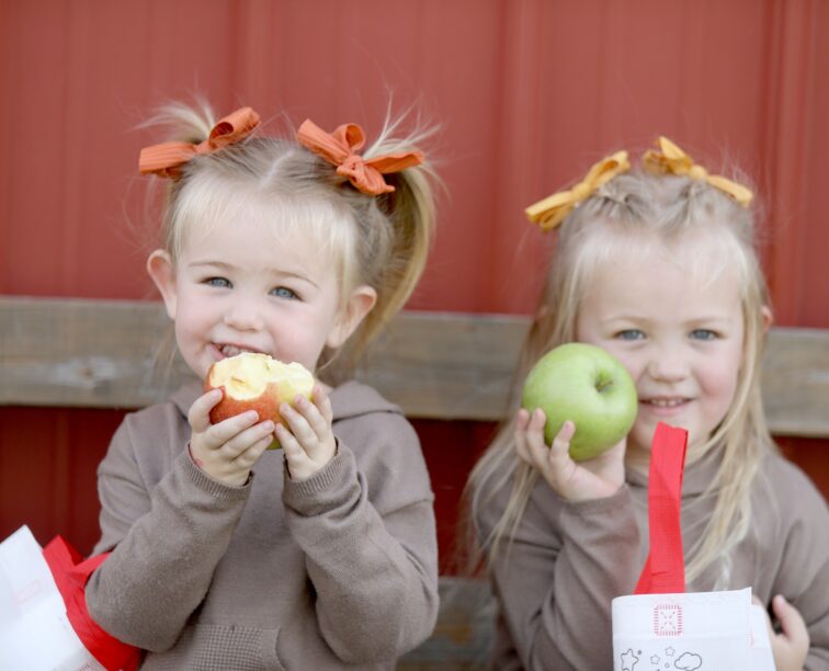 Two little girls snacking on apples they picked at Tanners Orchard